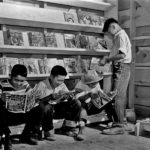 Four youth — confined to the War Relocation Authority center in Newel, Calif. — enjoy the latest comic books available at the newsstand in July 1942. In the upper right, issues of Fantastic Adventures (August 1942) and Wild West Weekly (June 20, 1942) await sale. Four youth — confined to the War Relocation Authority center in Newel, Calif. — enjoy the latest comic books available at the newsstand in July 1942. In the upper right, issues of Fantastic Adventures (August 1942) and Wild West Weekly (June 20, 1942) await sale.