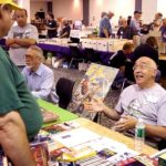 Ron Fortier, seated right, discusses his Captain Hazzard book as Don Hutchison, author of The Great Pulp Heroes, sits beside him at a dealer’s table.